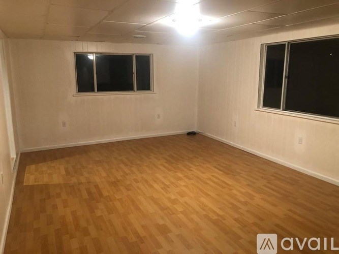 A room with wooden flooring and two windows.
