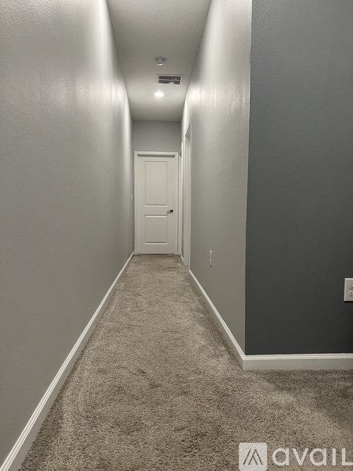 A long hallway with a carpeted floor and a white door at the end.