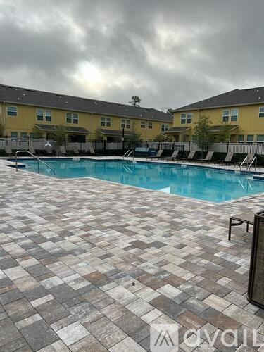 A pool surrounded by a tiled patio and apartment buildings in the background.