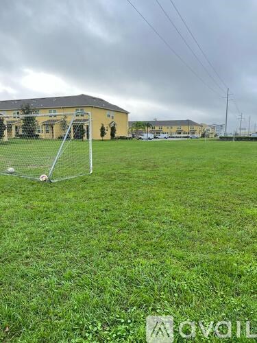 A soccer goal stands in a grassy field with a building in the background.