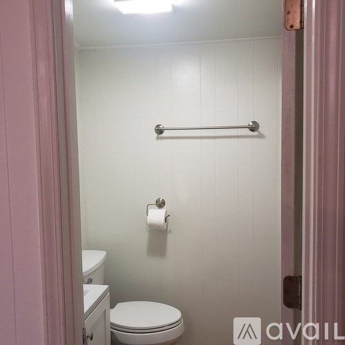 A white toilet is in a small bathroom with a towel rack and a roll of toilet paper on the wall.