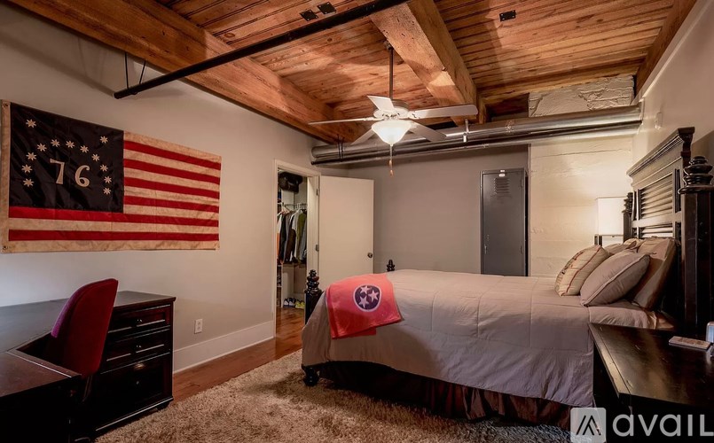 A bedroom with a bed, a chair, and an American flag on the wall.