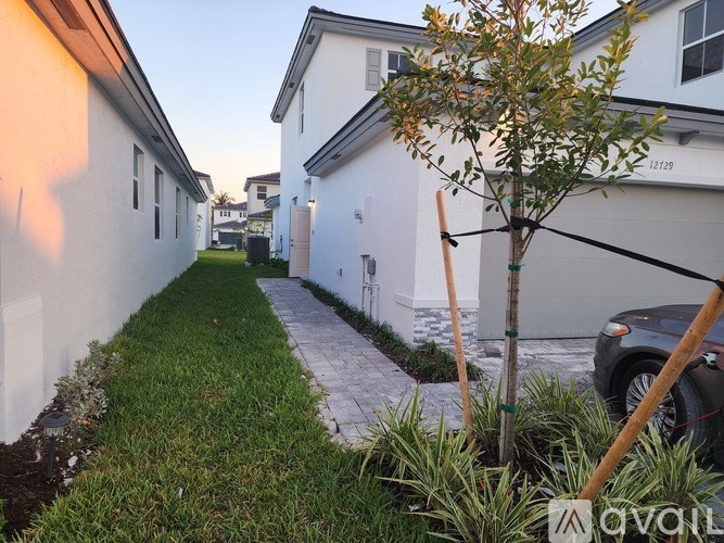 A tree in a yard with a white house in the background.