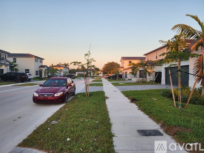 A red car is driving down a street with houses on both sides.