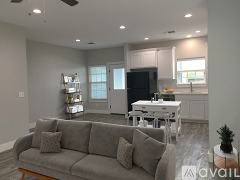 A living room with a grey couch and a kitchen area in the background.