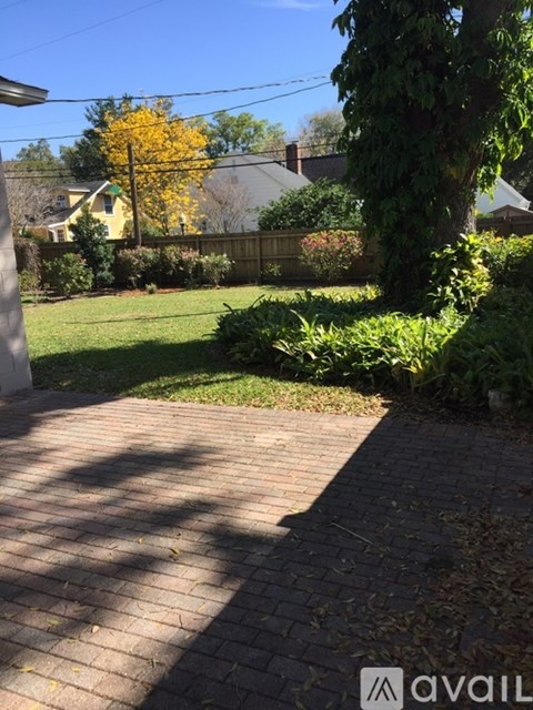 A backyard with a brick walkway and a tree with yellow leaves.