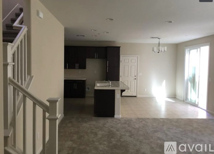 A spacious living room with a kitchen in the background and a staircase on the left.