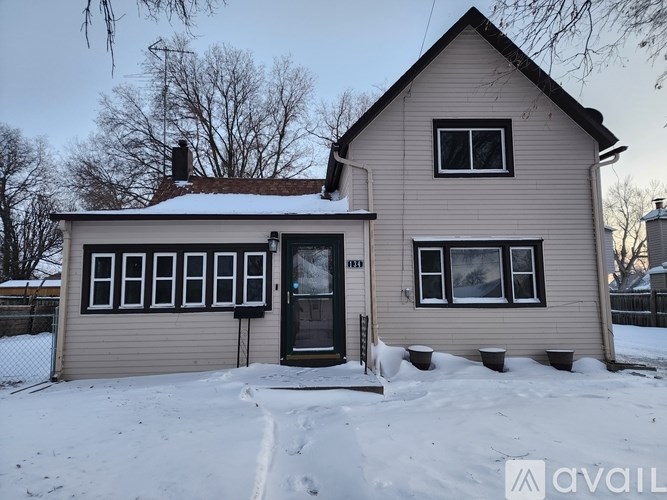 A house with a brown roof and a grey siding is surrounded by snow.