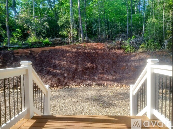 A white railing overlooks a dirt area with trees in the background.