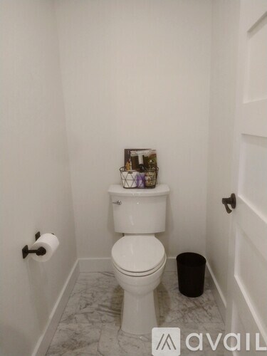 A white toilet in a bathroom with a black trash can and a toilet paper roller.
