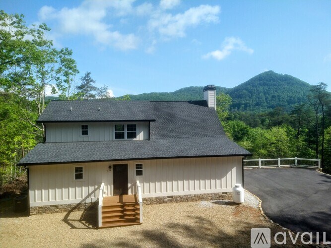 A white house with a black roof is surrounded by greenery.