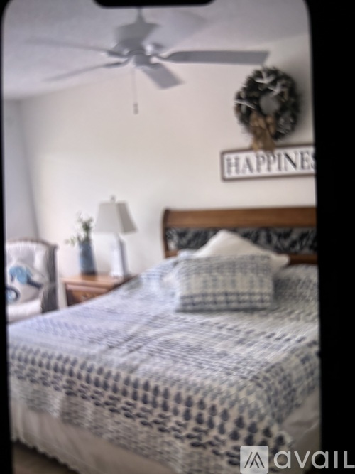 A bedroom with a bed, a chair, a ceiling fan, and a sign that says "HAPPINESS".