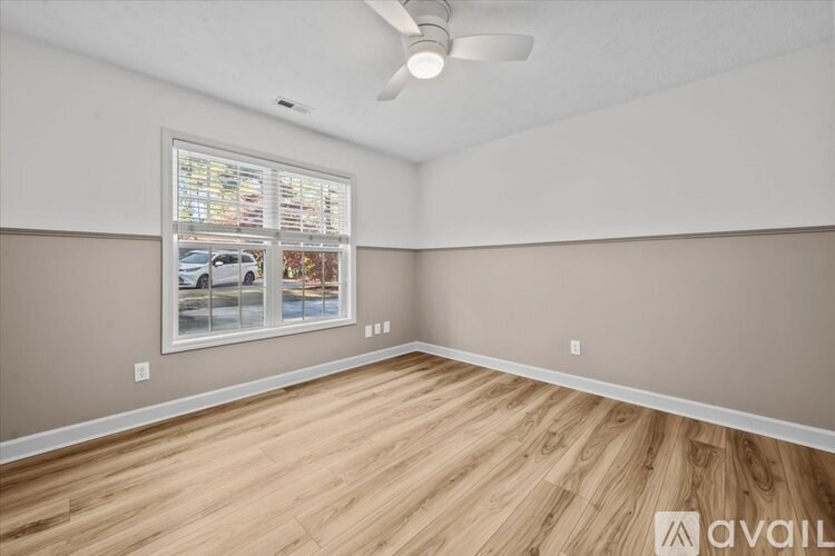 A room with a ceiling fan and a window showing a car and trees outside.