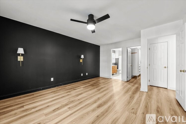 A room with black walls and wooden flooring, featuring a ceiling fan and two wall-mounted lights.