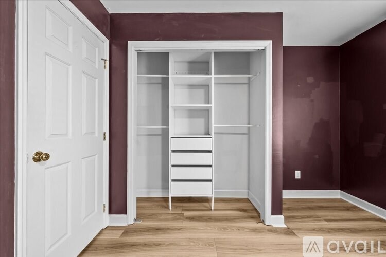 A white door is on the left of a room with a white shelving unit.