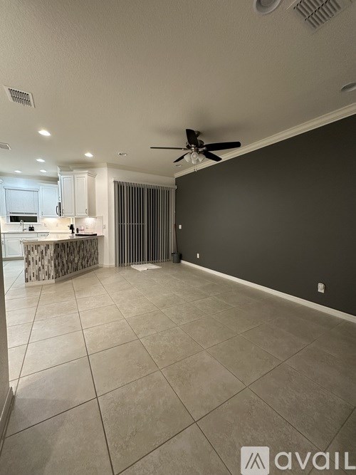 A spacious room with a ceiling fan and a kitchen area in the background.