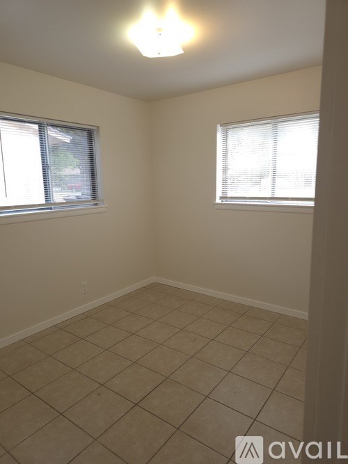 A room with tiled flooring and two windows.