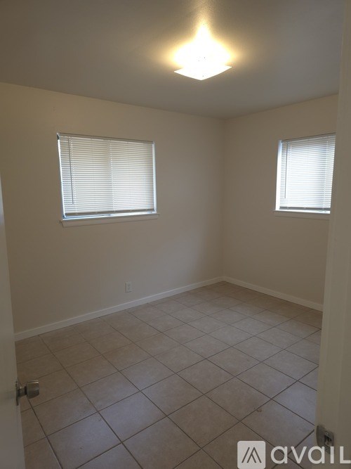 A room with tiled flooring and two windows with blinds.