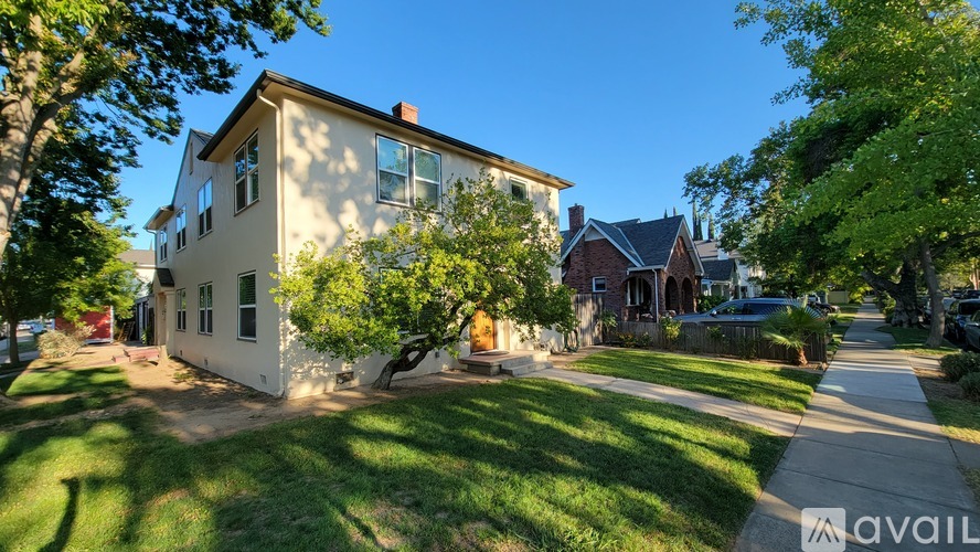 A house with a white facade is surrounded by greenery and other houses.