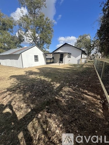 A white barn with a metal roof is surrounded by a fence and trees.