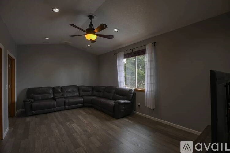 A living room with a black leather couch and a ceiling fan.