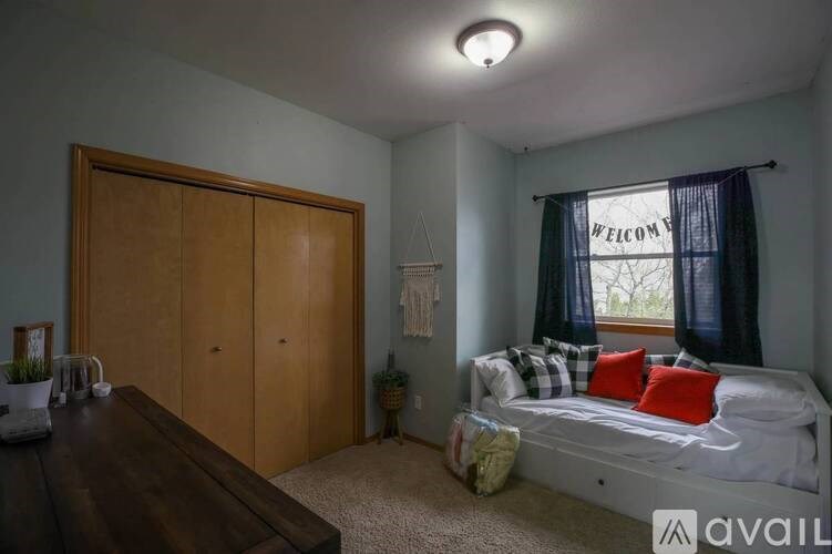 A bedroom with a bed, a window with a "Welcome" sign, and a wooden wardrobe.