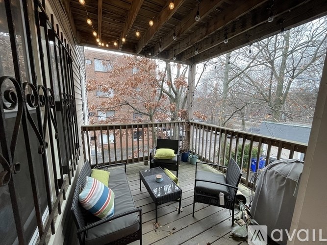 A balcony with a table and chairs overlooking a tree-lined street.