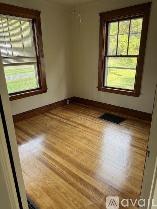 A room with wooden flooring and two windows.