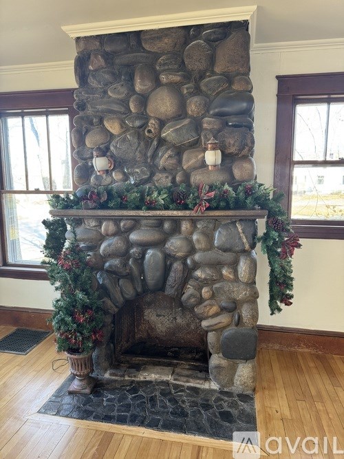 A stone fireplace with a garland and stockings hanging on it.