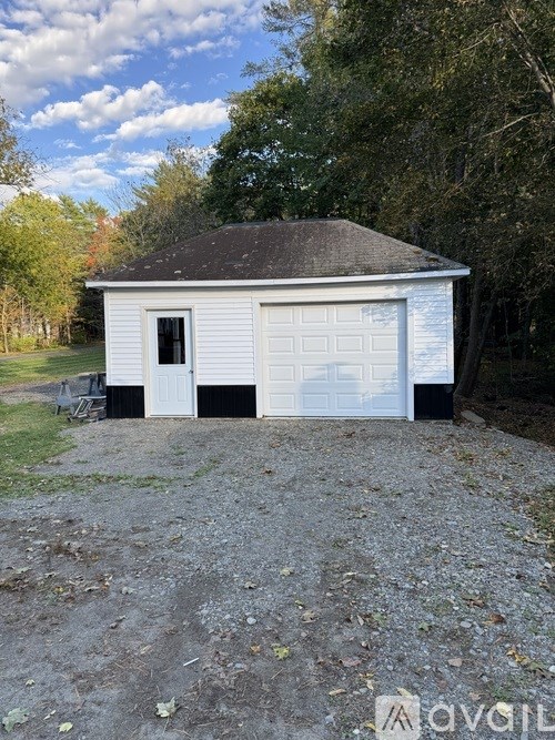 A white garage with a black roof is surrounded by trees.