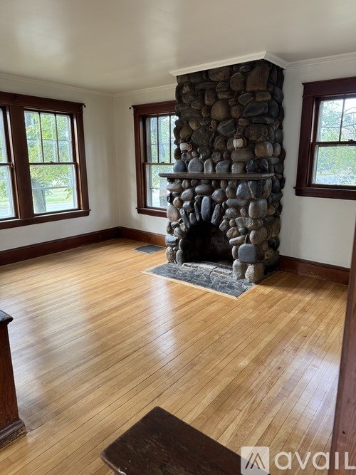 A stone fireplace in a room with wooden floors and windows.
