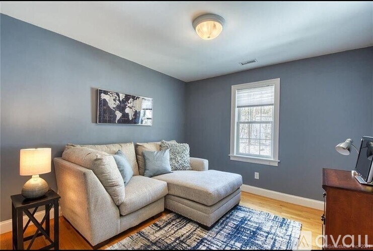 A living room with a grey couch, a lamp, a painting, and a window.