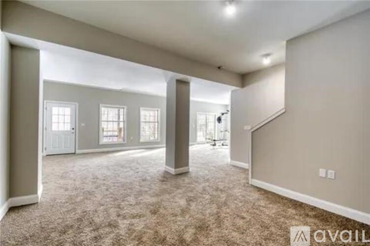 A spacious living room with a carpeted floor and a staircase on the right side.