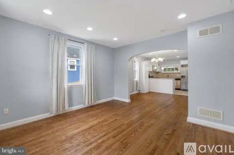 A spacious room with wooden flooring and a large window with curtains.