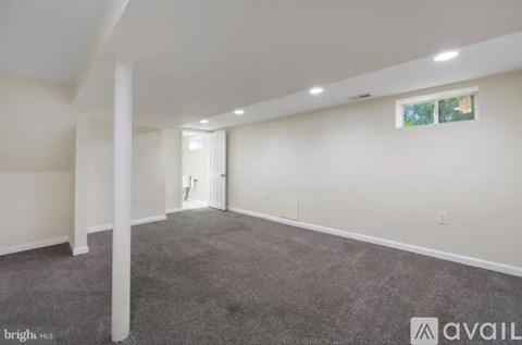 A spacious room with carpeted floor and white walls, with a doorway leading to another room.