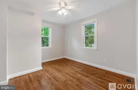 A room with wooden flooring and two windows.
