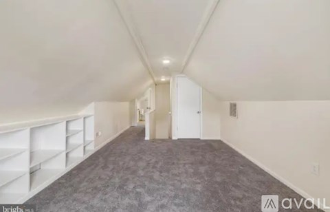 A spacious room with a carpeted floor and a staircase on the left side.