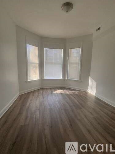 A room with wooden flooring and three windows.