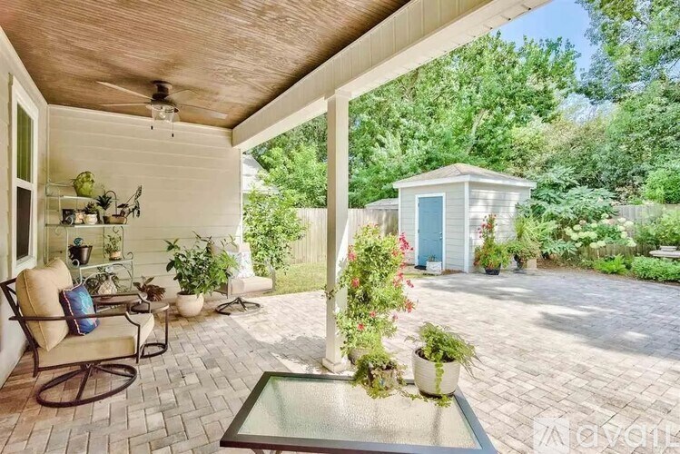 A patio with a table and chairs is surrounded by green plants.