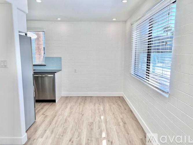 A kitchen with a refrigerator, a counter, and a window with blinds.