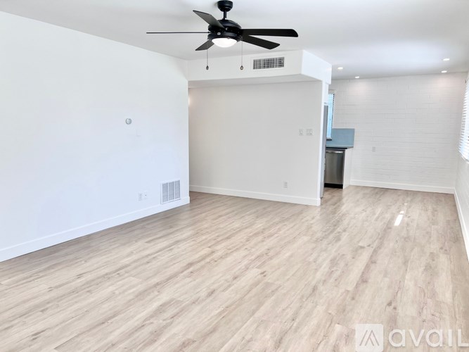 A spacious room with a ceiling fan and light fixture, and a wooden floor.