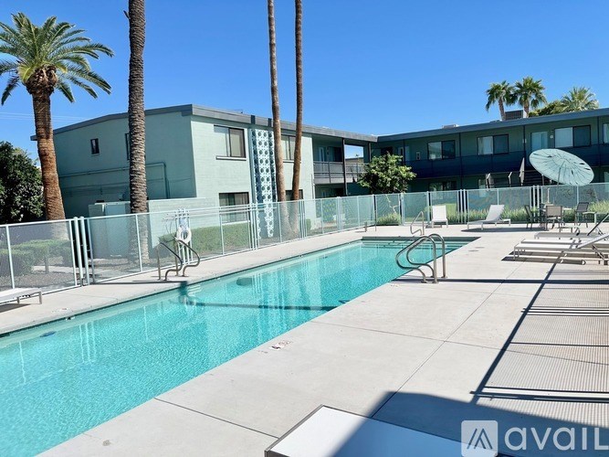 A pool surrounded by a fence and chairs with a building in the background.