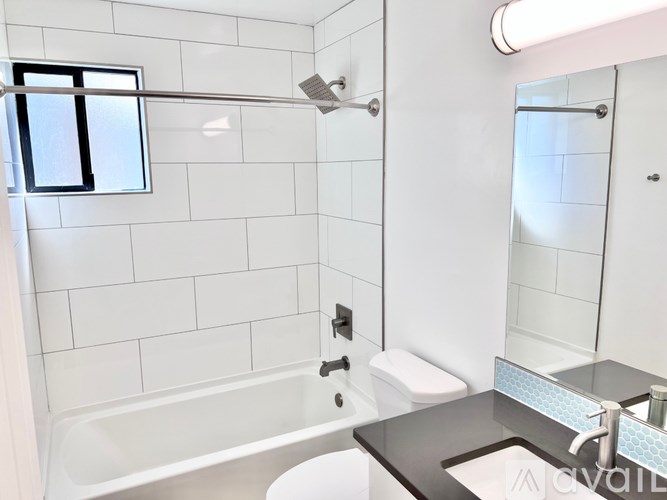 A white tiled bathroom with a black counter top and a white toilet.