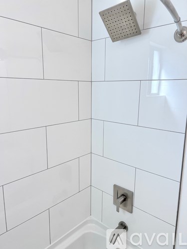 A white tiled shower with a silver shower head and faucet.