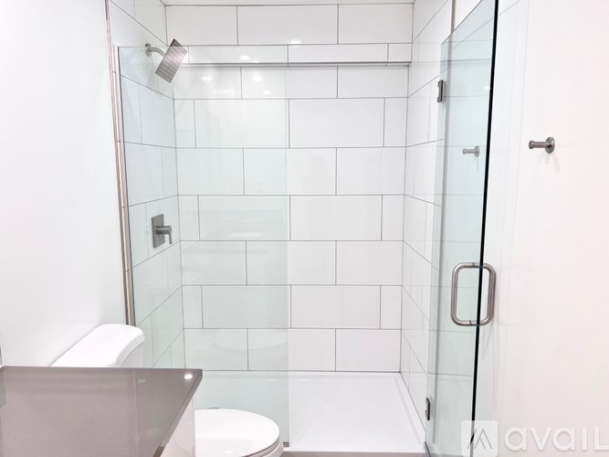 A white tiled shower with a glass door and a toilet.