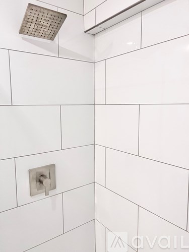 A white tiled shower with a silver shower head and handle.