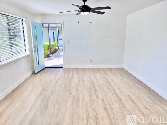 A room with a ceiling fan and light fixture, wooden flooring, and a door leading outside.