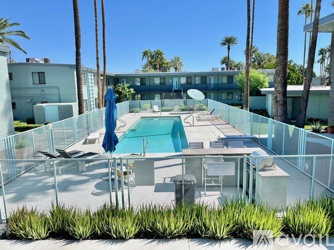 A pool surrounded by a fence with a blue umbrella and a chair.