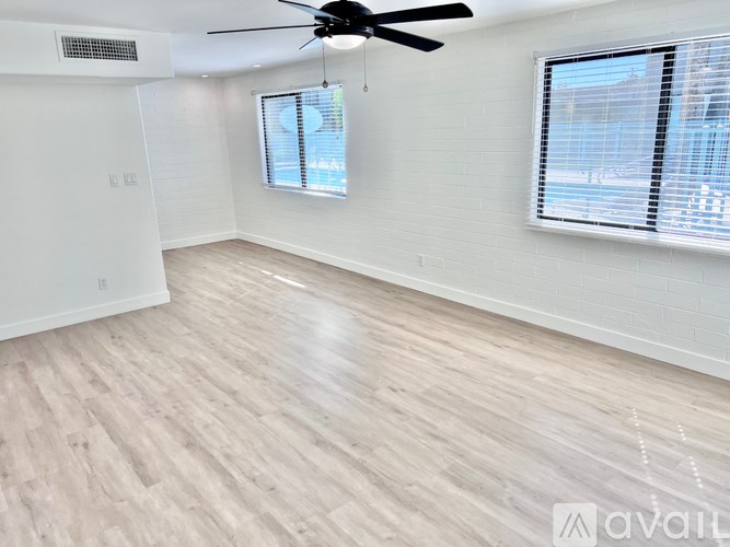 A room with a ceiling fan and light, hardwood floors, and a window with blinds.