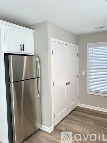 A stainless steel refrigerator in a kitchen with white cabinets and a white door.